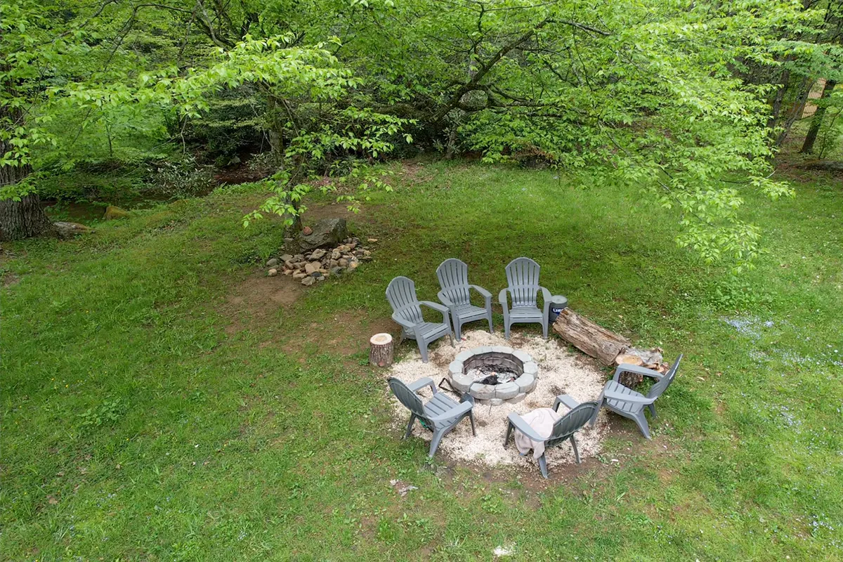 A classic fire pit area with adjoining chairs, nestled among tall trees for a cozy and communal outdoor experience. The space is perfect for gathering, storytelling, and roasting s’mores.