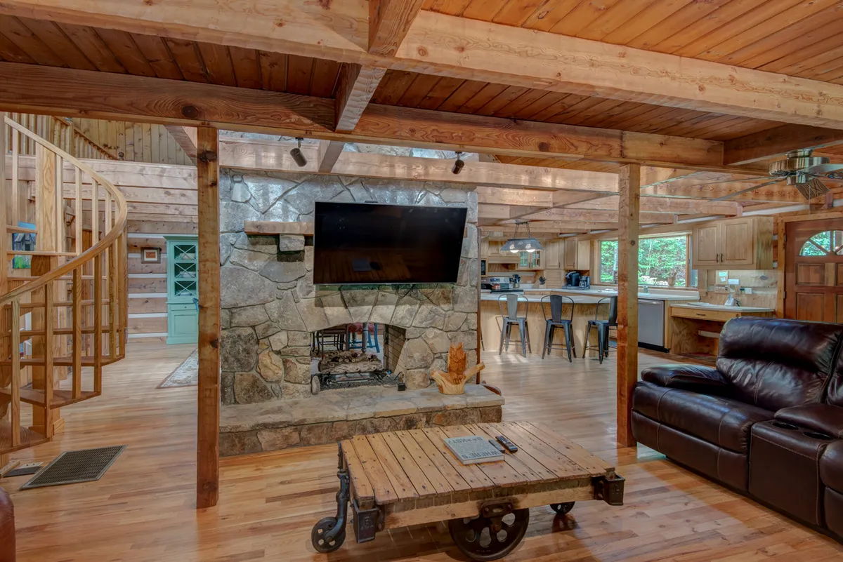 This image captures a warm and inviting living area with a stone fireplace, leather sofa, wooden table, and most importantly, a prominent spiral staircase leading upward. The open layout supports visibility between levels, aligning with the description of the loft overlooking the main space below.