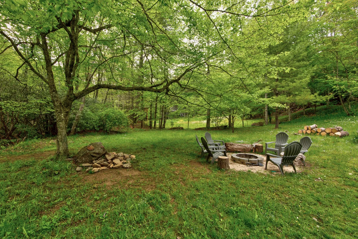 A cozy fire pit encircled by Adirondack chairs rests amid vibrant greenery. The scene suggests an ideal spot for evening fireside chats, storytelling, and stargazing with friends or loved ones.