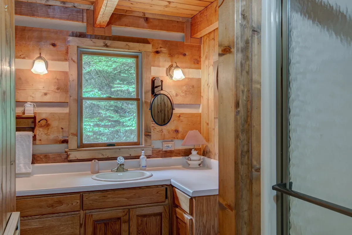 A warm and inviting attached bathroom with wooden cabinetry, a sink and mirror, and a window with a green, natural view. The space offers both functionality and a peaceful atmosphere for self-care routines.