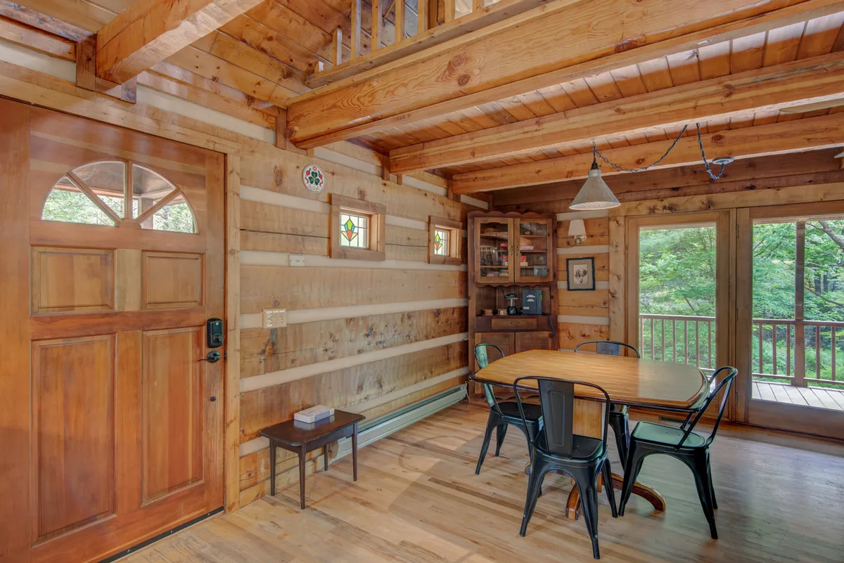A bright dining space with a large wooden table, surrounded by windows and stained glass, sits adjacent to a welcoming kitchen area. The table is set to accommodate games, puzzles, or family meals, and the sliding glass doors offer easy access to the outdoors, further enhancing the room’s inviting atmosphere.